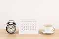 Calendar, alarm clock and cup of coffee on table