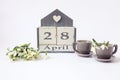 Calendar for April 28: cubes with the number 28, the name of the month in English, two gray coffee cups, a bouquet of snowdrops on Royalty Free Stock Photo