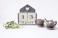 Calendar for April 13: cubes with the number 13, the name of the month in English, two gray coffee cups, a bouquet of snowdrops on Royalty Free Stock Photo