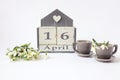 Calendar for April 16: cubes with the number 16, the name of the month in English, two gray coffee cups, a bouquet of snowdrops on Royalty Free Stock Photo