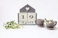 Calendar for April 19: cubes with the number 19, the name of the month in English, two gray coffee cups, a bouquet of snowdrops on Royalty Free Stock Photo
