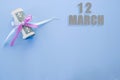 Calendar date on blue background with rolled up dollar bills pinned by blue and pink ribbon with copy space. March 12 is the