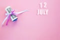 Calendar date on pink background with rolled up dollar bills pinned by pink and blue ribbon with copy space. July 12 is the