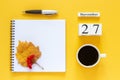 Calendar November 27 cup of coffee, notepad with pen and yellow leaf on yellow background Royalty Free Stock Photo