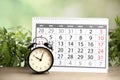 Calender and alarm clock on wooden table against green background