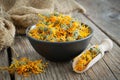 Calendula flowers in bowl, wooden scoop of dry marigold petals and canvas sack on background. Herbal medicine