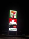 A sign of a Seven Eleven, Petro Canada with the price of gas and a Car Wash sign at night. A Royalty Free Stock Photo