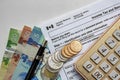 Canadian Tax Forms with coins, calculator, a pen and bills on a white table. Tax time