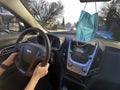 A person driving a Chevrolet car on a sunny day, with a face mask hanging from the mirror.