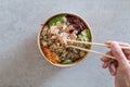 California Poke Bowl with salmon, avocado, crab surimi, carrot, red cabbage, ginger, sushi rice and cucumber. Man hands shown.