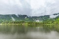 Caling spring summer foggy lake. Evergreen pine forest and mountain line under clouds and fog Royalty Free Stock Photo