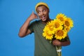 Call me. Gesturing handsome African American young man, guy with armful of sunflowers wearing khaki, green t-shirt and yellow hat