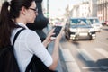 Call a taxi using the mobile application. A young woman in the city is standing near the road with a smartphone Royalty Free Stock Photo