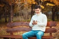 Call to me or write a message! Handsome young man in sweater and jeans using smartphone while sitting on the bench Royalty Free Stock Photo