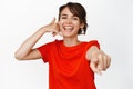 Call us. Smiling pretty girl pointing finger at camera, laughing and showing mobile phone gesture near ear, red t-shirt Royalty Free Stock Photo