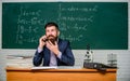 Calling parents. School teacher call mobile phone while sit classroom chalkboard background. Teacher bearded man talk