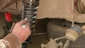 The calloused hands of a mechanic twist the coil spring ties with a wrench during DIY car repairs.