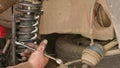 The calloused hands of a mechanic twist the coil spring ties with a wrench during DIY car repairs.