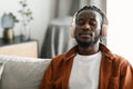 Calm african american man in wireless headphones sitting on sofa with closed eyes and listening to music, free space Royalty Free Stock Photo