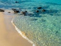 Calm beach scene, movement of blue sea water and wave surf, group of rocks on clean sandy beach. Royalty Free Stock Photo