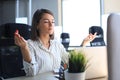 Calm beautiful businesswoman practicing yoga at work, meditating in office with eyes closed