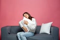 Calm beautiful young girl embracing pillow with closed eyes relaxing, resting, feeling sleepy, sitting on cozy couch