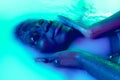 Close up female face of african girl in milk bath with soft white glowi in neon light. Modern neoned colors, foam