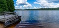 Calm blue lake in the middle of the forest with a wooden dock and rowboat in the foreground Royalty Free Stock Photo