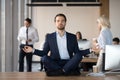 Calm businessman in suit meditating in office on work desk