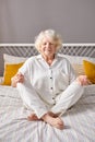 calm caucasian senior woman engaged in yoga, sit on bed with crossed legs