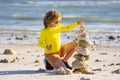 Calm child play with pyramid stones balance on the sand of the beach. Kid with stack of stones on sand near sea. Child Royalty Free Stock Photo