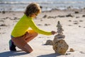 Calm child play with pyramid stones balance on the sand of summer beach. Child play with stack of stones. Child play on