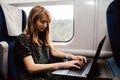 Calm concentrated young woman work in train during travelling. Typing on laptop keyboard. Sit alone in wagon at window Royalty Free Stock Photo