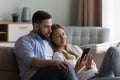 Calm couple in love holding mobile phone on home sofa