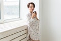 Calm and coziness. Beautiful young woman with cup of tea standing near the window at home Royalty Free Stock Photo