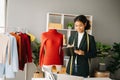 Calm curly brunette dark skinned woman on desk in office of fashion designer and holds tablet and smartphone