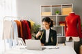 Calm curly brunette dark skinned woman on desk in office of fashion designer and holds tablet and smartphone