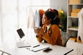 Calm curly brunette dark skinned woman on desk in office of fashion designer and holds tablet and smartphone