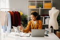 Calm curly brunette dark skinned woman on desk in office of fashion designer and holds tablet and smartphone