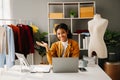 Calm curly brunette dark skinned woman on desk in office of fashion designer and holds tablet and smartphone