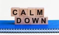 CALM DOWN - a word made of wooden blocks with black letters, a row of blocks is located on a blue Notepad. White background, front Royalty Free Stock Photo