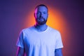 Close up portrait of young caucasian bearded man  on dark studio background in neon lights. Royalty Free Stock Photo