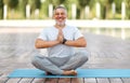 Calm happy mature man sitting in lotus pose on mat during morning meditation in park Royalty Free Stock Photo