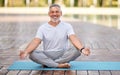Calm happy senior man sitting in lotus pose on mat during morning meditation in park