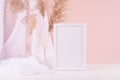 Calm home decor with blank photo frame for text, silk curtain, fluffy reeds bouquet on white wood table, pink wall. Template. Royalty Free Stock Photo