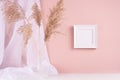 Calm home decor with square blank photo frame for text hanging on pink wall, silk curtain, fluffy reeds bouquet on white wood. Royalty Free Stock Photo