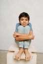 Calm indian boy sitting on a wooden box, hugging his knees.