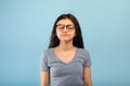 Calm Indian teen girl posing with closed eyes, meditating or praying to God over blue studio background