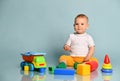Calm infant baby boy toddler in yellow pants is sitting surrounded by colorful toys on background with copy space