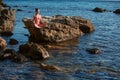 Calm lady in pink bikini meditating on rock. Calm sea. Alone time. Meditation and self-absorbed. Spare time outdoors